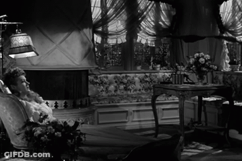 A Woman Sits In A Chair In Front Of A Fireplace In A Black And White Photo GIF