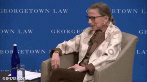 A Woman Sits In A Chair In Front Of A Georgetown Law Backdrop GIF