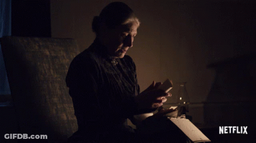 A Woman Sits In A Dark Room Reading A Book With A Netflix Logo On The Bottom GIF