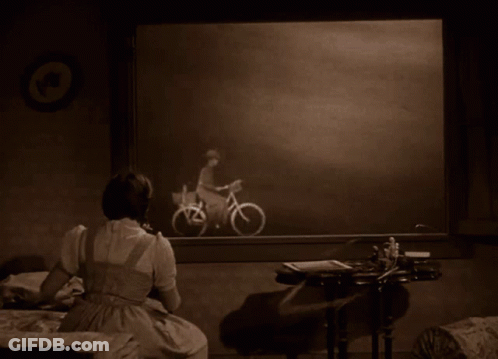 A Woman Sits In Front Of A Picture Of A Man Riding A Bicycle GIF