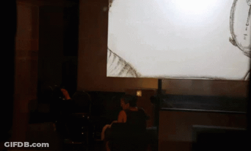 A Woman Sits In Front Of A Projector Screen That Shows A Drawing GIF