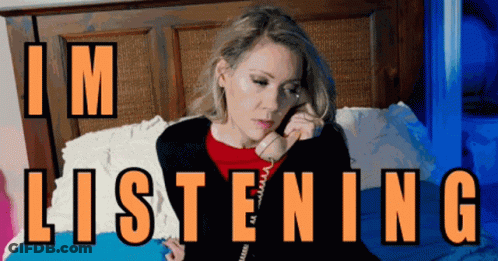 A Woman Sits On A Bed Talking On A Phone With The Words " I 'M Listening " Written Above Her GIF