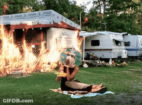 A Woman Sits On A Blanket In Front Of A Rv That Is On Fire GIF