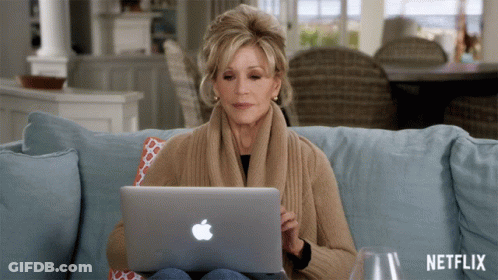 A Woman Sits On A Couch Using An Apple Laptop With Netflix Written On The Bottom GIF