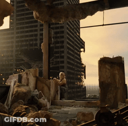 A Woman Sits On A Pile Of Rocks In Front Of A City Skyline GIF