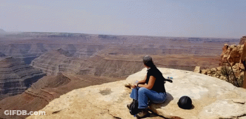 A Woman Sits On A Rock Overlooking A Desert Landscape GIF