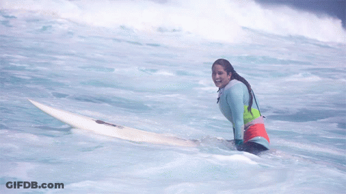A Woman Sits On A Surfboard In The Ocean And Smiles GIF