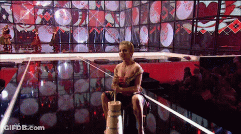 A Woman Sits On A Wooden Barrel In Front Of A Screen That Says 05 Poland On It GIF