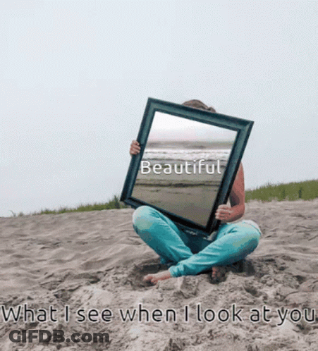 A Woman Sits On The Beach Holding A Picture Frame With The Word Beautiful On It GIF