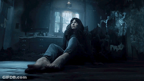 A Woman Sits On The Floor In A Dark Room Looking Up GIF