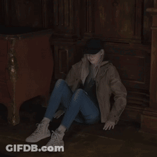 A Woman Sits On The Floor Wearing A Hat And Jeans GIF