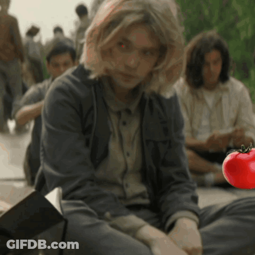 A Woman Sits On The Ground With A Red Tomato In The Foreground GIF