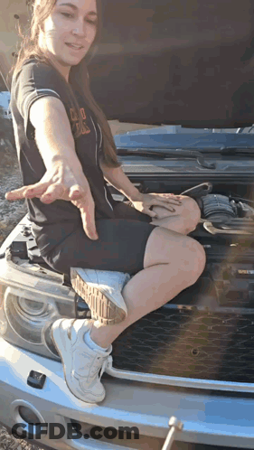 A Woman Sits On The Hood Of A Car With The Hood Open GIF