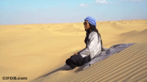A Woman Sits On Top Of A Sand Dune GIF
