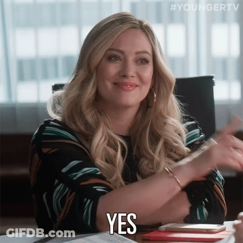 A Woman Sitting At A Desk Says Yes With Her Hands GIF