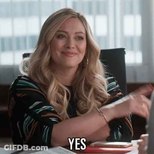 A Woman Sitting At A Desk With The Word Yes On Her Chest GIF
