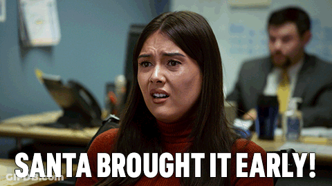 A Woman Sitting At A Desk With The Words Santa Brought It Early On The Bottom GIF