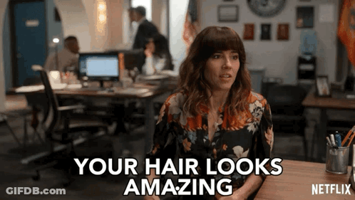 A Woman Sitting At A Desk With The Words " Your Hair Looks Amazing " On The Screen GIF
