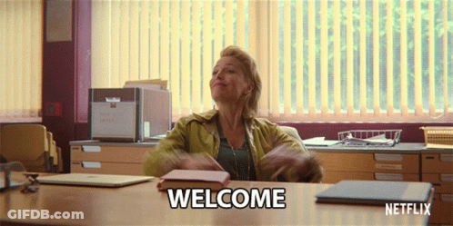 A Woman Sitting At A Desk With Welcome Written On The Table GIF
