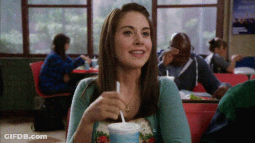 A Woman Sitting At A Table Drinking A Milkshake GIF