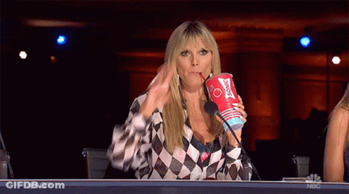 A Woman Sitting At A Table Drinking From A Cup That Says Sonic GIF