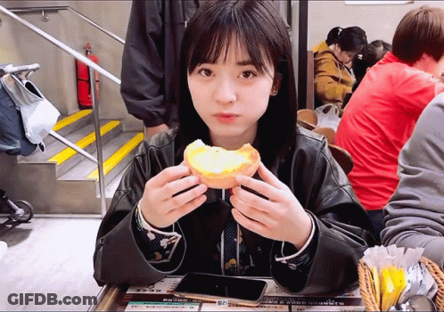 A Woman Sitting At A Table Eating A Sandwich With A Sign That Says ' A ' On It GIF
