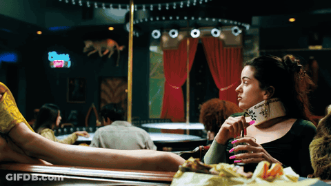 A Woman Sitting At A Table In A Bar Holding A Purse That Says ' Swag ' On It GIF