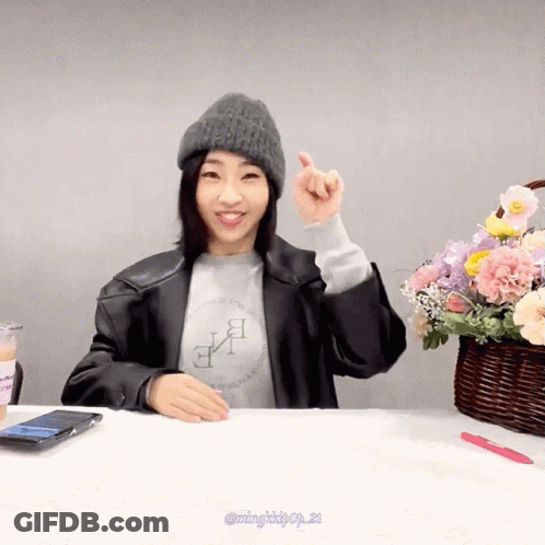 A Woman Sitting At A Table With A Basket Of Flowers GIF