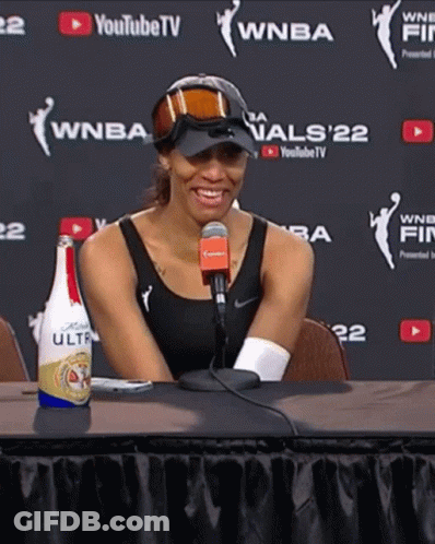A Woman Sitting At A Table With A Bottle Of Bud Light Ultra On It GIF