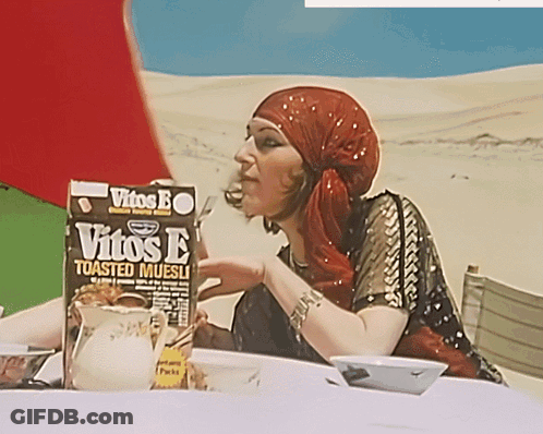 A Woman Sitting At A Table With A Box Of Vitos E Toasted Muesli In Front Of Her GIF