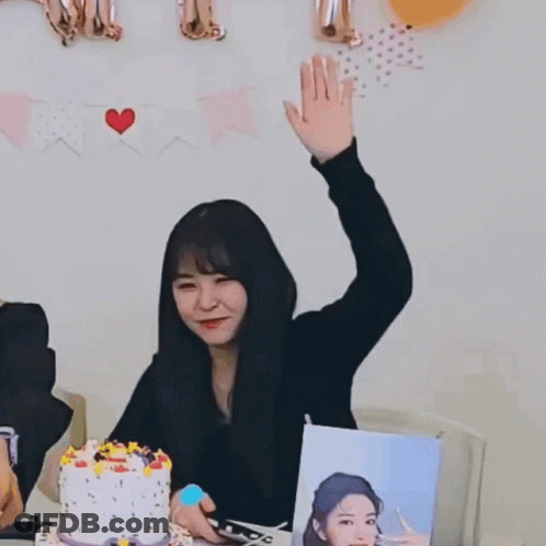 A Woman Sitting At A Table With A Cake And Balloons Behind Her With A Sign That Says " I Love You " GIF