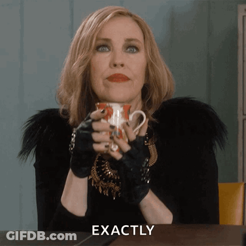 A Woman Sitting At A Table With A Cup In Her Hand And The Word Exactly Written Below Her GIF