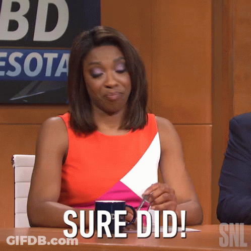 A Woman Sitting At A Table With A Cup Of Coffee And A Sign That Says Snl GIF