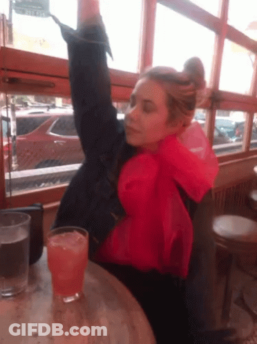 A Woman Sitting At A Table With A Glass Of Orange Liquid GIF