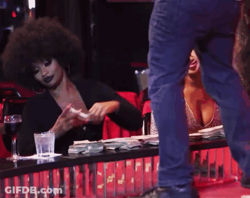 A Woman Sitting At A Table With A Glass Of Water And A Man Standing Behind Her GIF