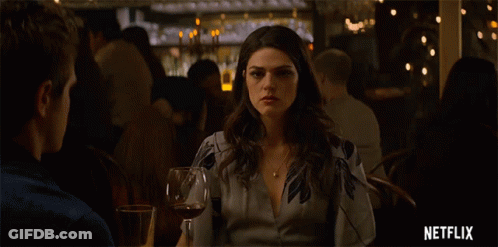 A Woman Sitting At A Table With A Glass Of Wine And A Netflix Logo GIF