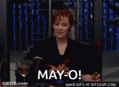 A Woman Sitting At A Table With A Glass Of Wine And The Words May-O GIF