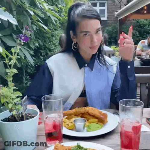 A Woman Sitting At A Table With A Plate Of Food GIF
