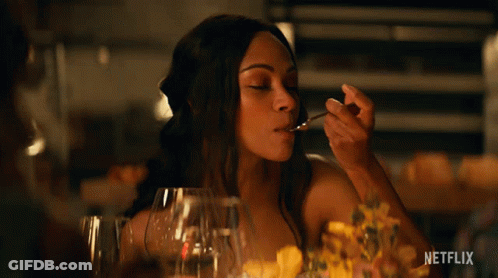 A Woman Sitting At A Table With A Spoon In Her Mouth And The Word Netflix On The Bottom Right GIF