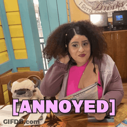 A Woman Sitting At A Table With A Stuffed Animal And The Word Annoyed On The Bottom GIF