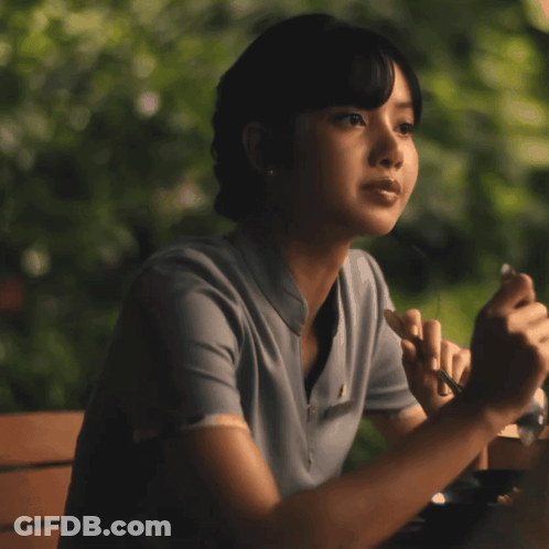 A Woman Sitting At A Table With Her Eyes Closed Holding A Pen GIF