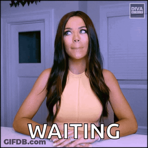 A Woman Sitting At A Table With The Word Waiting Written On The Screen GIF