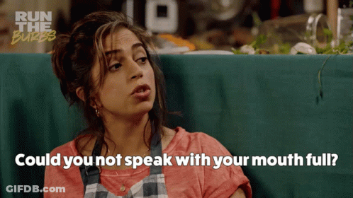 A Woman Sitting At A Table With The Words " Could You Not Speak With Your Mouth Full " Written Below Her GIF
