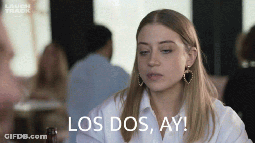 A Woman Sitting At A Table With The Words Los Dos Ay Written On Her Face GIF