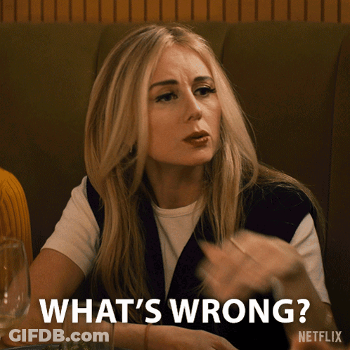 A Woman Sitting At A Table With The Words What 'S Wrong On The Bottom GIF