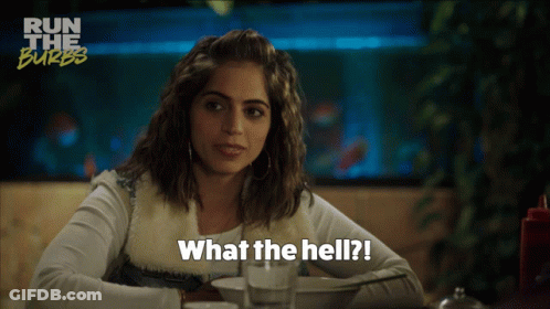 A Woman Sitting At A Table With The Words " What The Hell " On The Bottom GIF