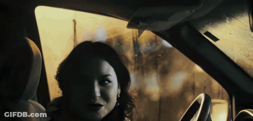 A Woman Sitting In A Car Looking Out The Window At The Camera GIF