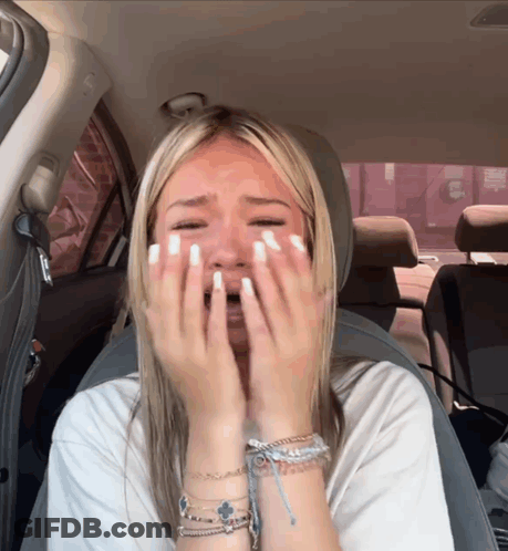 A Woman Sitting In A Car With Her Hands On Her Face GIF