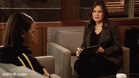 A Woman Sitting In A Chair Talking To Another Woman While Holding A Clipboard GIF