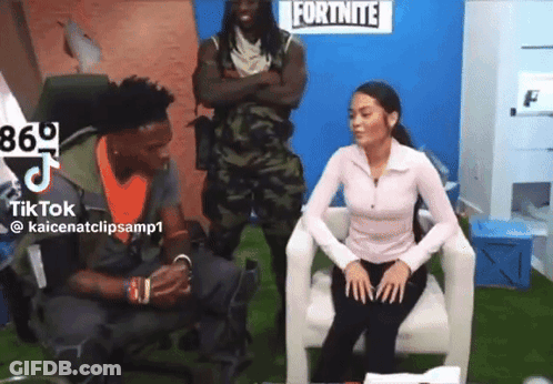 A Woman Sitting In A Chair With A Man Standing Behind Her In Front Of A Fortnite Sign GIF